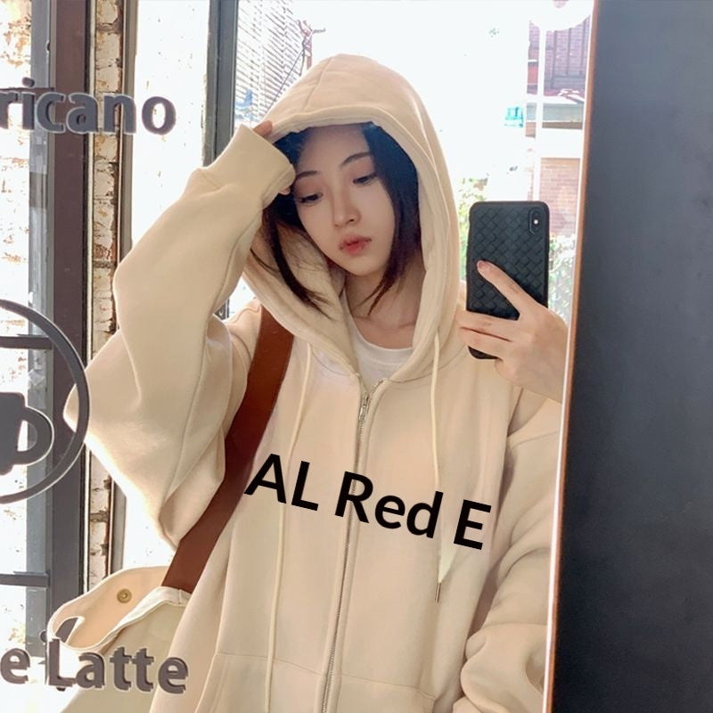 Young woman in a cream zip-up loose casual hoodie with hood up, taking a mirror selfie with a brown shoulder bag.