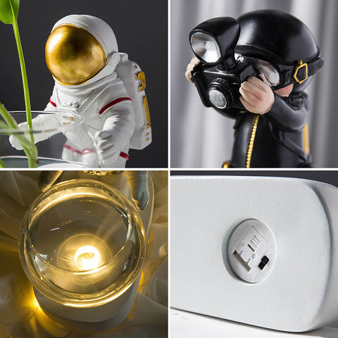 Gold-visor astronaut and green silver-diver resin figures with a glass hydroponic flowerpot and LED-lit base.