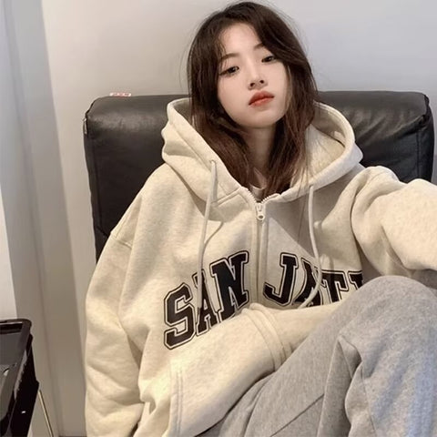 Woman in cream zip-up oversized casual-style hoodie with bold varsity lettering.