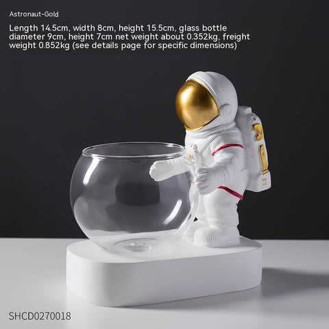 Astronaut gold visor decoration with hydroponic glass flowerpot on white base for tabletop decor.